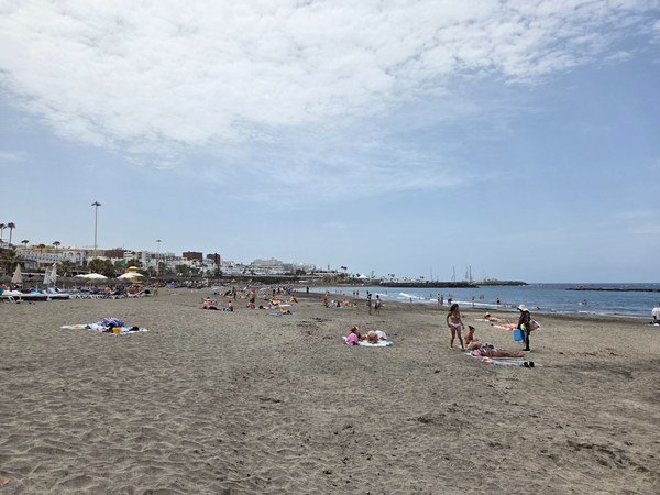 Playa de Fañabé con amplia franja de arena oscura, bañistas dispersos y hoteles en la zona costera.