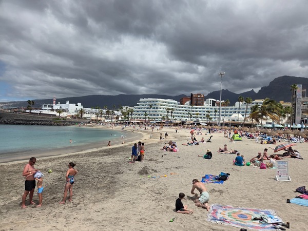 Playa de La Pinta en Costa Adeje con arena clara, bañistas, hoteles y cielo cubierto.