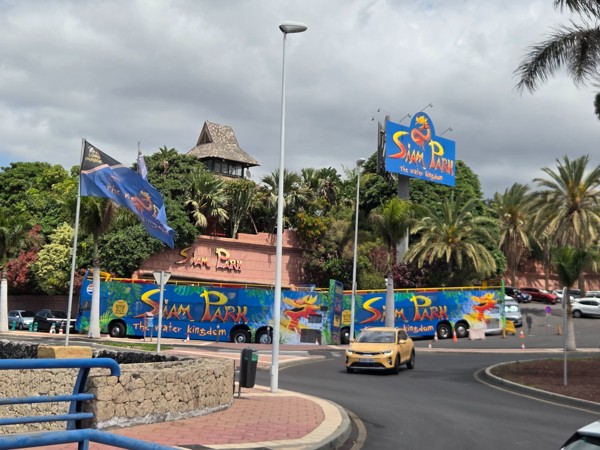 Entrada de Siam Park en Costa Adeje con carteles coloridos, vegetación tropical y autobuses turísticos.